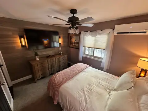 Bedroom 4 queen bed with dark wood headboard, mauve walls, sheer curtains and warm bedside lamps
