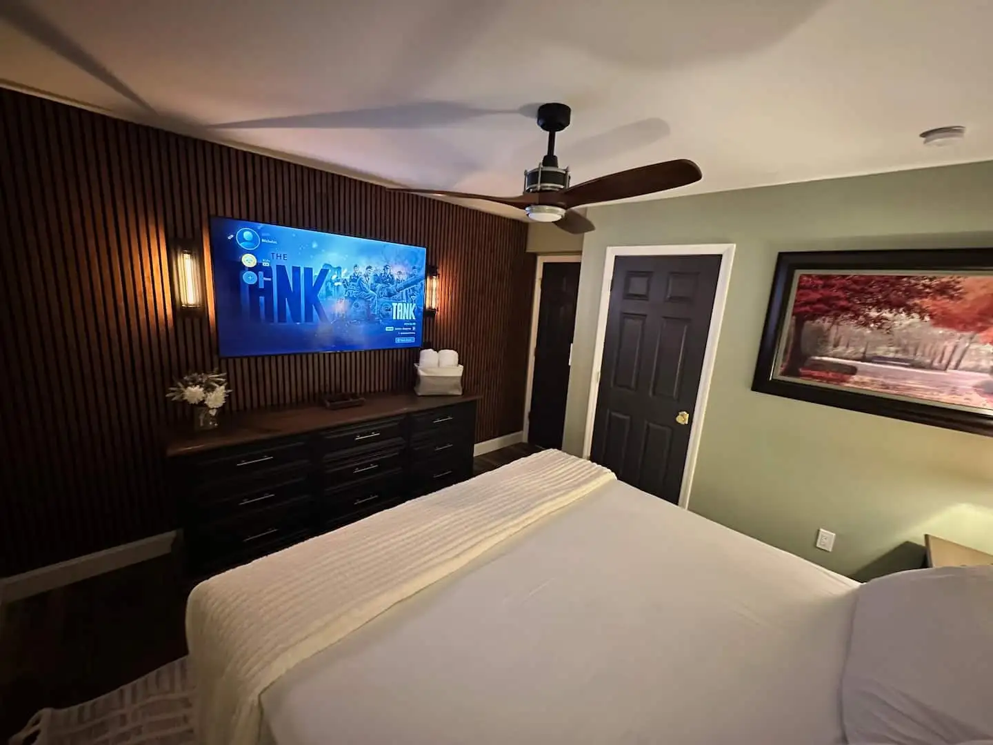 Bedroom 1 with wood slat accent wall, wall-mounted smart TV over a black dresser, and sconce lighting