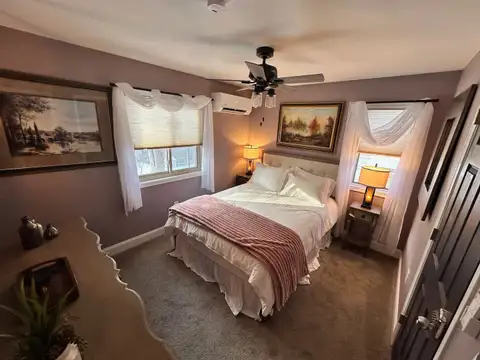 Bedroom 4 bed with blush throw, framed landscape art, sheer-draped windows and soft lamp light