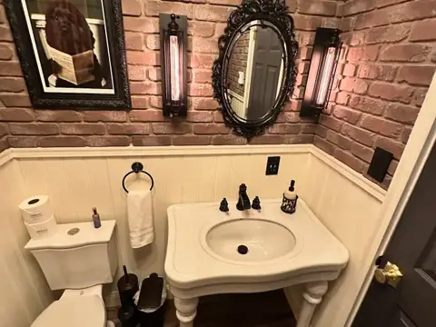 Speakeasy-style half bath with exposed brick, ornate black mirror, Edison sconces and vintage console sink