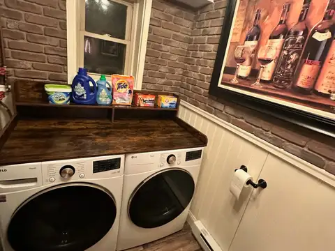 Half bath laundry nook with LG front-load washer and dryer, folding counter, brick walls and wine art