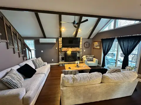 Living room with exposed beams, stone fireplace with wall-mounted TV, and two oversized cream sofas