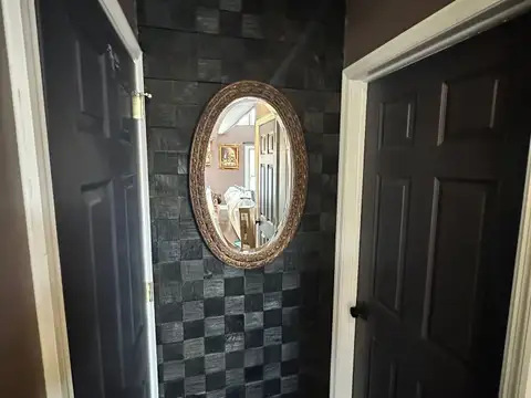 Hallway nook with black textured checkerboard accent wall, ornate oval gold-framed mirror and dark charcoal doors