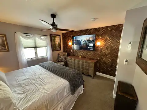 Bedroom 3 king bed facing a smart TV on a herringbone wood accent wall with globe sconces and armchair