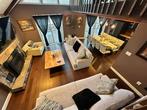 View from the loft over the living room's stone fireplace, cream sofas, and eight-seat dining table
