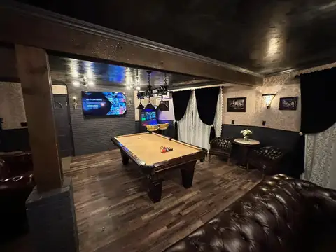 Pool table and brown leather couches under antique brass pendants in the moody, damask-papered game room