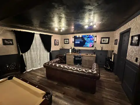 Game room wet bar with copper sink, beverage fridge and coffee maker behind a leather sofa and wall-mounted TV