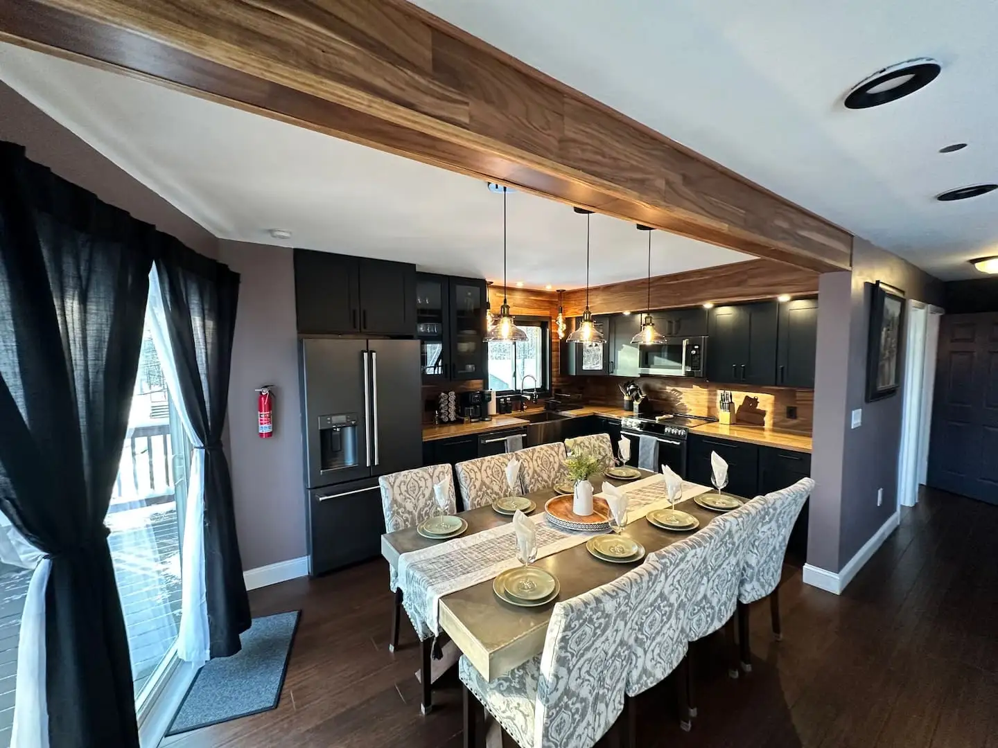 Full kitchen with matte-black appliances, butcher-block counters, wood accent beam, and elegantly set dining table