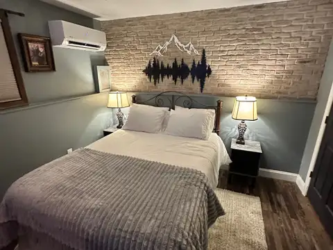 Bedroom 2 queen bed beneath a whitewashed brick wall with mountain and forest metal art and warm lamps