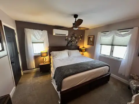 Bedroom 3 with plush white bedding, pink throw, wood-look accent wall, smart TV and glass-jar ceiling fan light