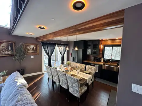 Dining table set for eight beside the kitchen with black cabinets, farmhouse sink, and pendant lighting
