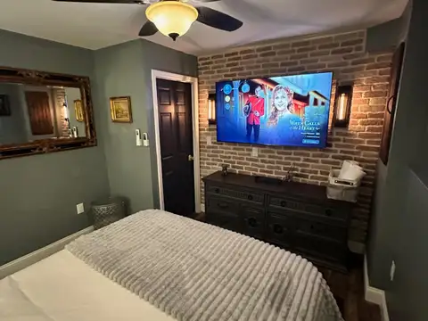 Bedroom 2 with smart TV and Edison sconces on an exposed brick wall above a dark vintage dresser