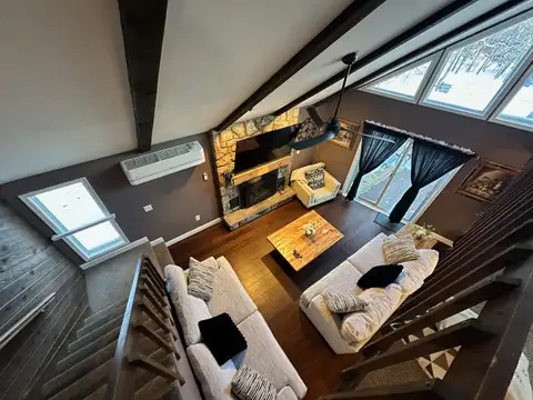 Loft view of the living room, wood coffee table, stone fireplace, and snowy woods through tall windows