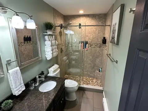 Full bathroom with double granite vanity, glass walk-in shower with pebble floor and plush white towels