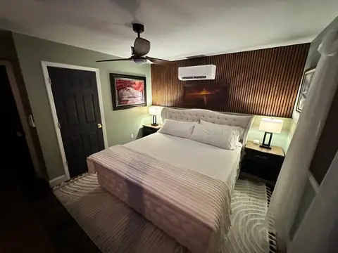 Bedroom 1 king bed with tufted headboard against a wood slat wall, sage green walls and bedside lamps