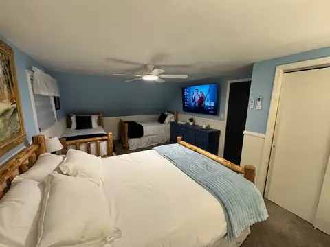 Bedroom 5 with king log bed, two twin log beds, wall-mounted smart TV and ceiling fan in soft blue tones