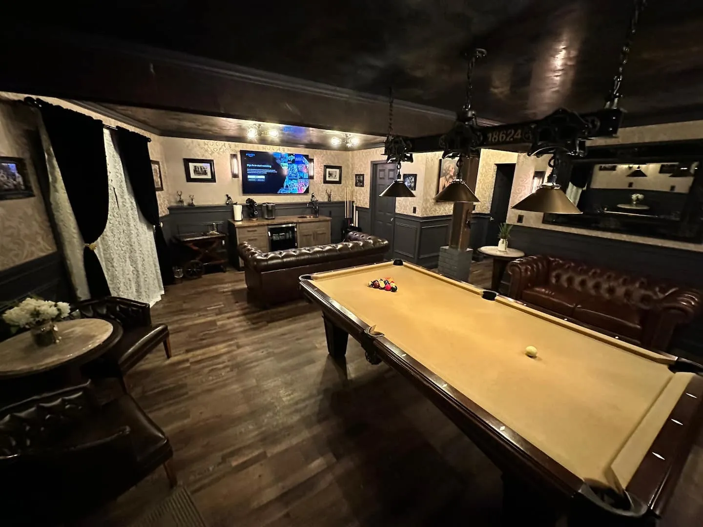Speakeasy-style game room with pool table under brass 18624 pendant lights, leather sofas and smart TV