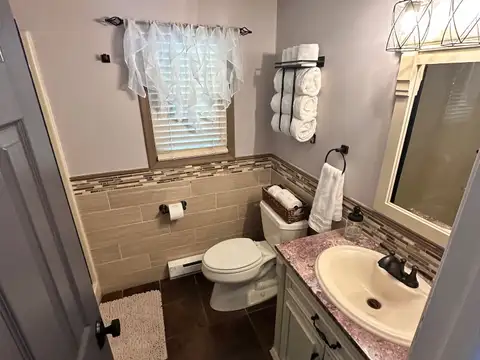 Full bathroom with cream vanity, rose granite top, wood-look tile wainscoting and rolled white towels