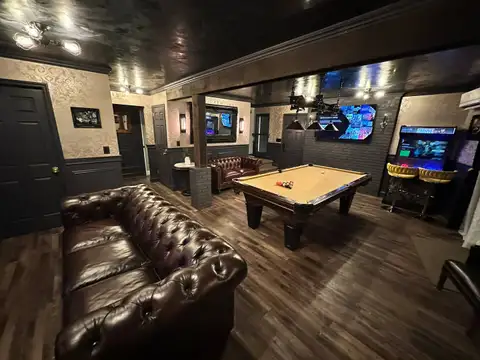 Tufted leather Chesterfield sofa facing the pool table, arcade cabinet and bar stools in the game room