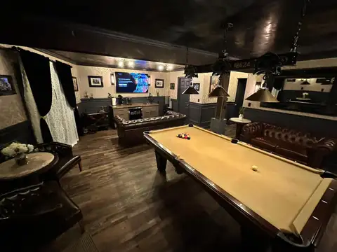 Wide view of the game room's pool table, exposed beam, arcade corner and leather seating on dark wood floors