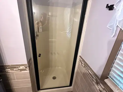 Corner glass-door shower stall in the second full bathroom with matte black fixtures and soft bath mat