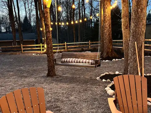 Backyard porch swing under glowing string lights at dusk, framed by tall trees and Adirondack chairs