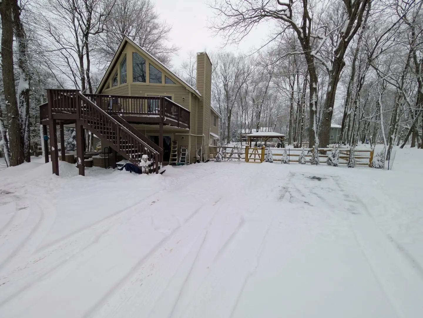 Snow-covered chalet with wraparound wooden deck, tall prow windows, and chimney amid wintry Poconos trees