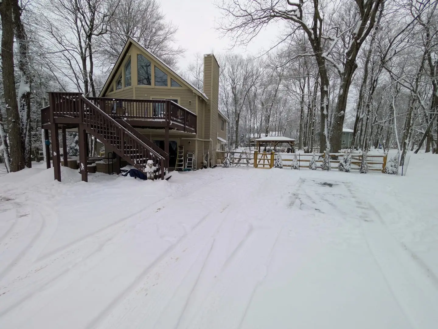 Snow-covered chalet with wraparound wooden deck, tall prow windows, and chimney amid wintry Poconos trees