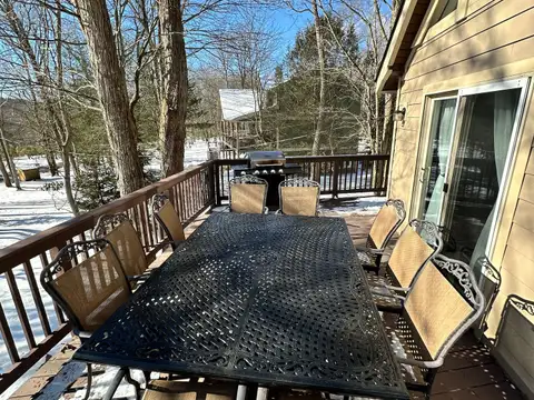 Back deck with wrought-iron dining table for ten and gas grill overlooking snowy woods on a sunny day