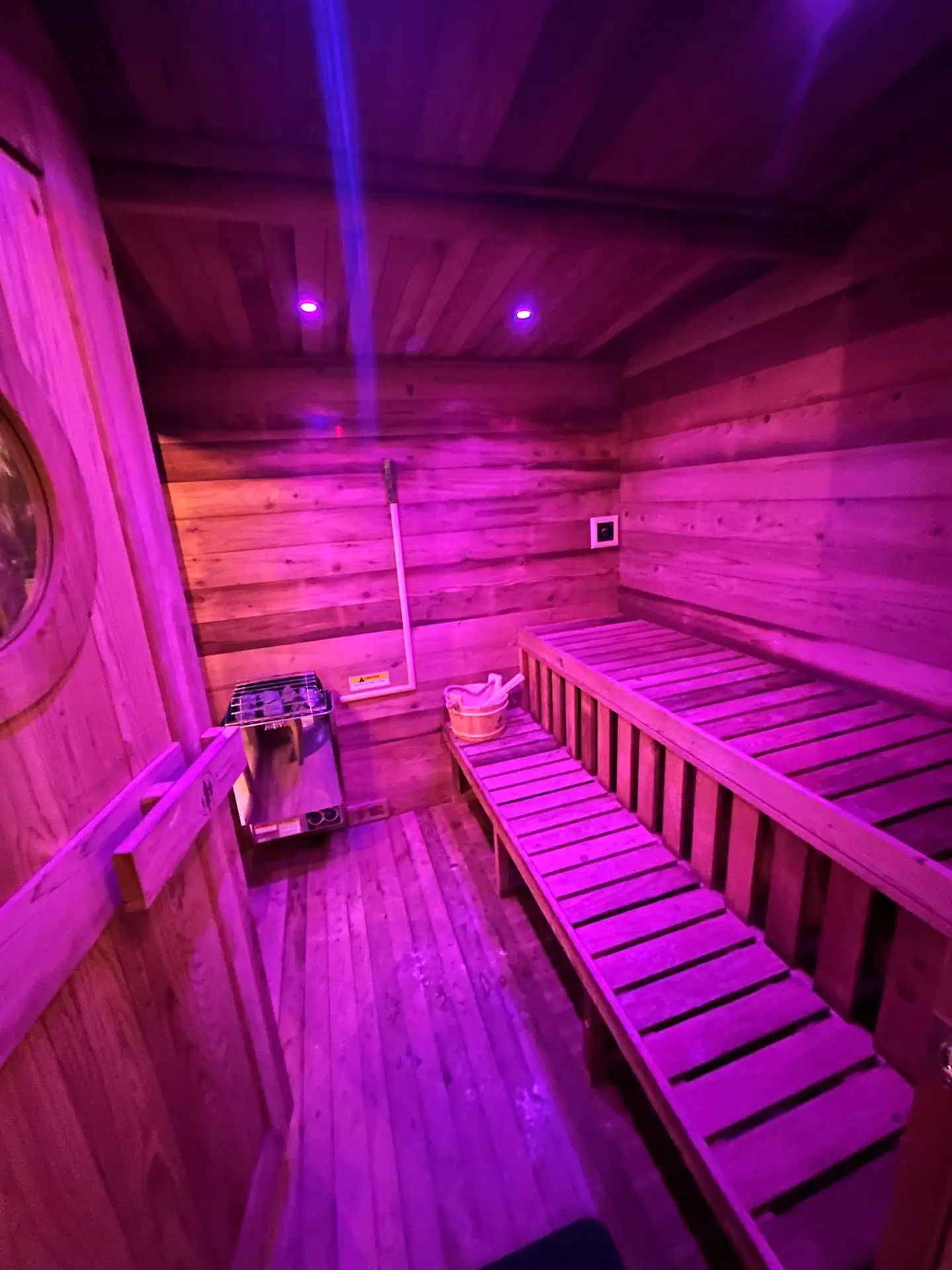 Cedar sauna interior glowing with purple mood lighting, tiered bench seating, wooden bucket and heater