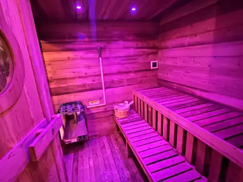 Cedar sauna interior glowing with purple mood lighting, tiered bench seating, wooden bucket and heater