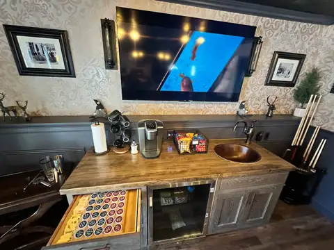 Game room wet bar with copper sink, Keurig, K-cup drawer, beverage fridge and wall-mounted TV over damask wallpaper