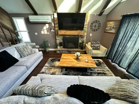 Stone fireplace with rustic wood mantel and large TV anchoring the living room's plush seating and shag rug