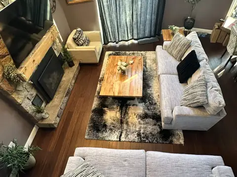 Bird's-eye view of the living room with plush cream sofas, stone fireplace, big-screen TV, and soaring windows