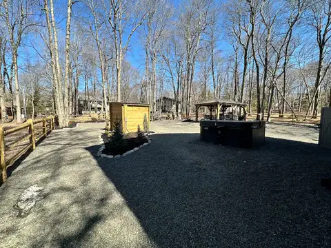 Sunny gravel backyard with private hot tub, cedar sauna cabin and wooden gazebo among bare trees