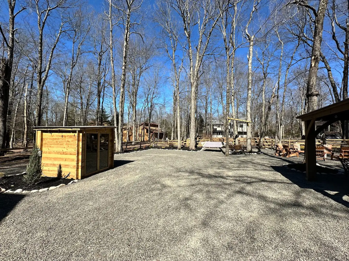 Fenced backyard with cedar sauna, hammock swing, and Adirondack chairs beside the covered gazebo