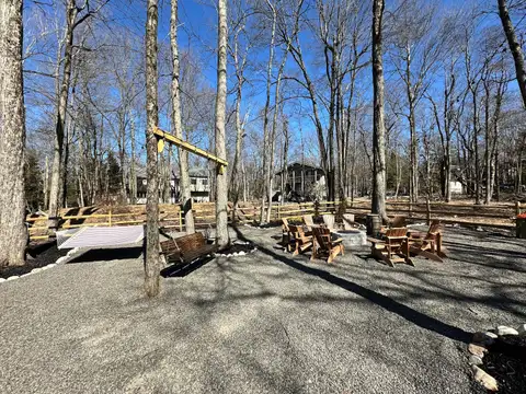 Backyard fire pit ringed by Adirondack chairs, with a hammock and hanging porch swing among the trees