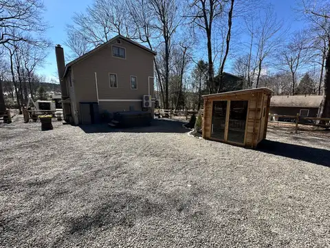 Rear of the chalet with outdoor hot tub and cedar sauna cabin on a wide gravel yard