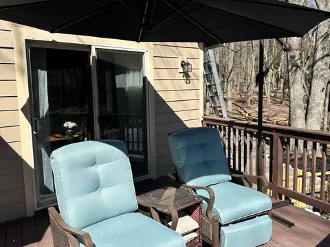 Two reclining chairs with teal cushions under a black cantilever umbrella on the sunny wooden deck