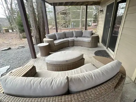 Covered patio with curved wicker sectional sofas and round ottoman overlooking the wooded front yard