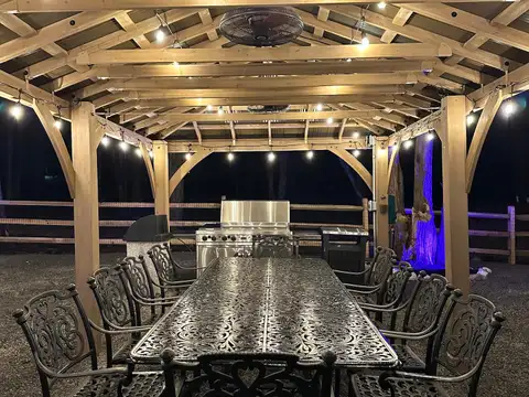 Ten-seat wrought-iron dining table beneath the gazebo's lit timber rafters, grill station glowing behind