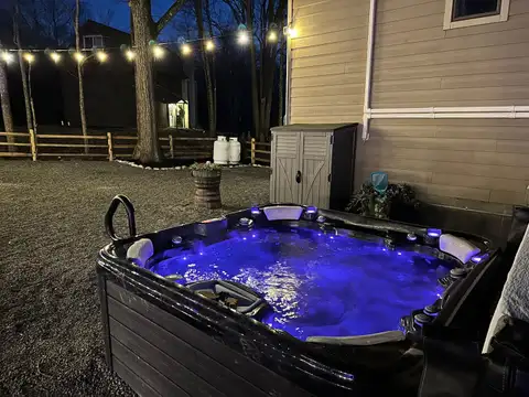 Bubbling hot tub glowing blue at night beside the chalet, with string lights over the fenced backyard