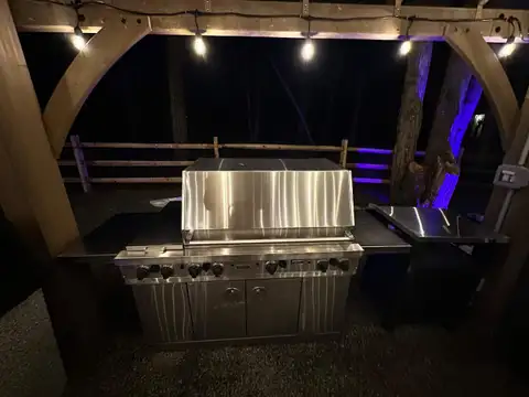 Stainless steel Viking grill under a timber-frame pavilion with string lights glowing in the backyard at night