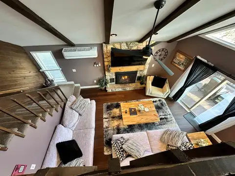 Living room from above with a glowing gas fireplace, ceiling fan, shag rug, and snowy deck out the glass doors